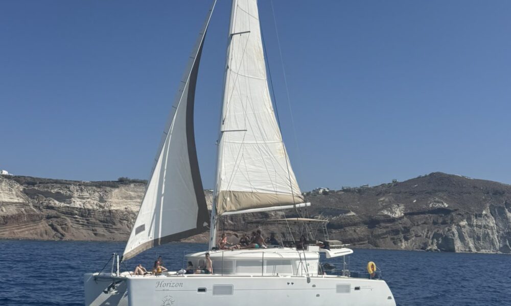 A white sailing boat cruising near the cliffs of Santorini during a sunny Santorini boat tour.