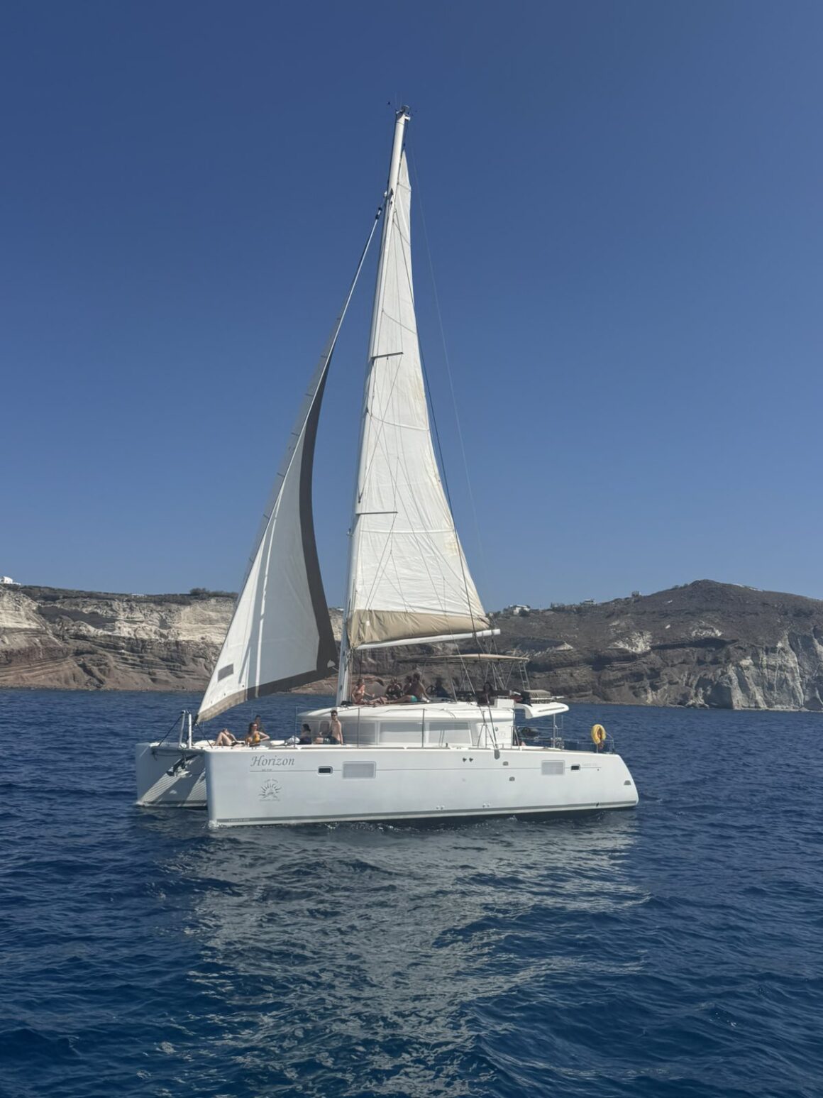 A white sailing boat cruising near the cliffs of Santorini during a sunny Santorini boat tour.