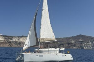 A white sailing boat cruising near the cliffs of Santorini during a sunny Santorini boat tour.